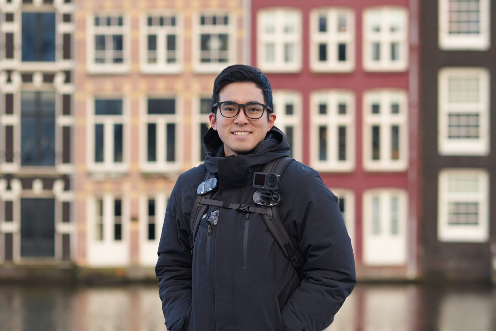 Portrait of Keiji, founder of Everyhuman Studio, standing by a canal with a small camera on his backpack strap