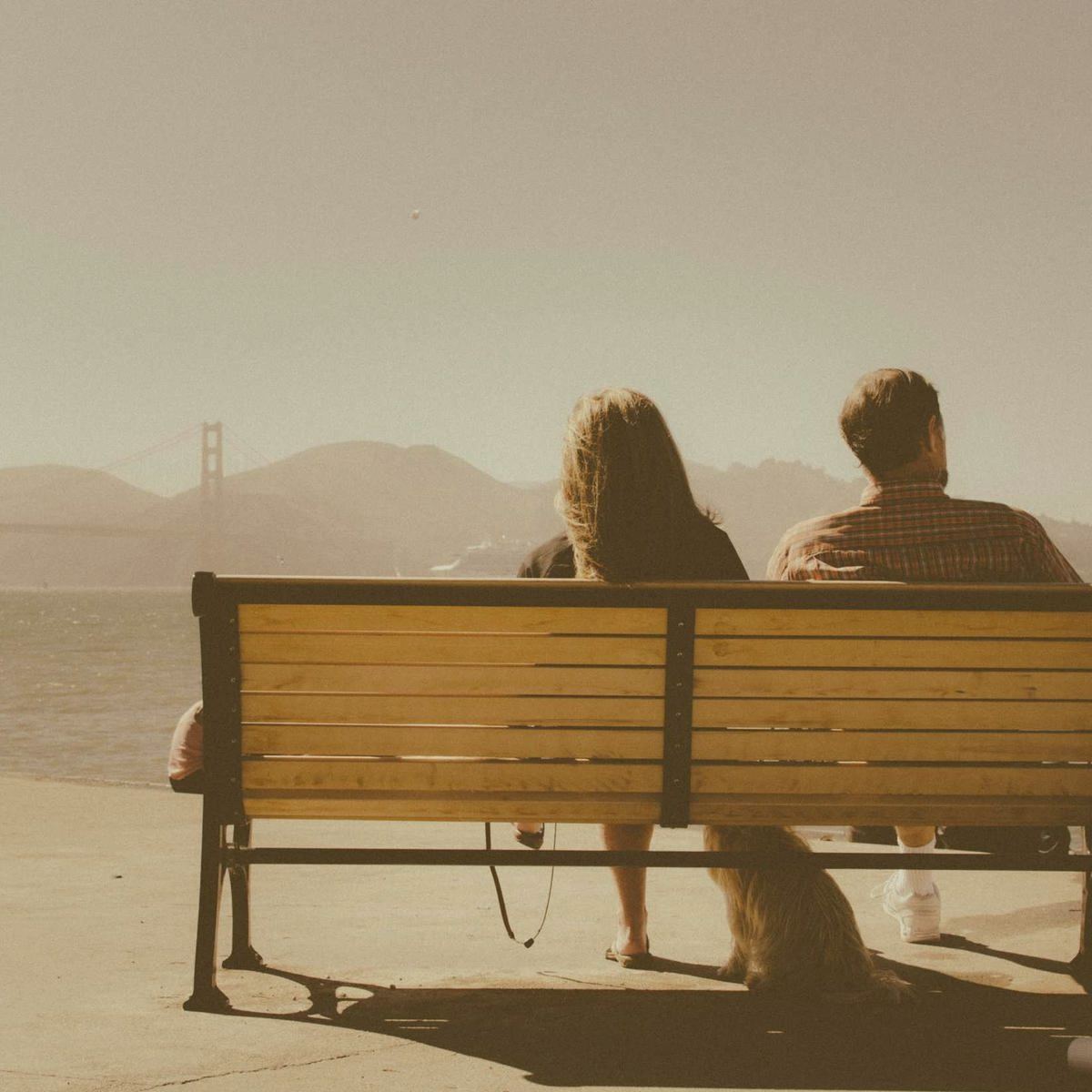 Two people sitting on a bench looking out over water